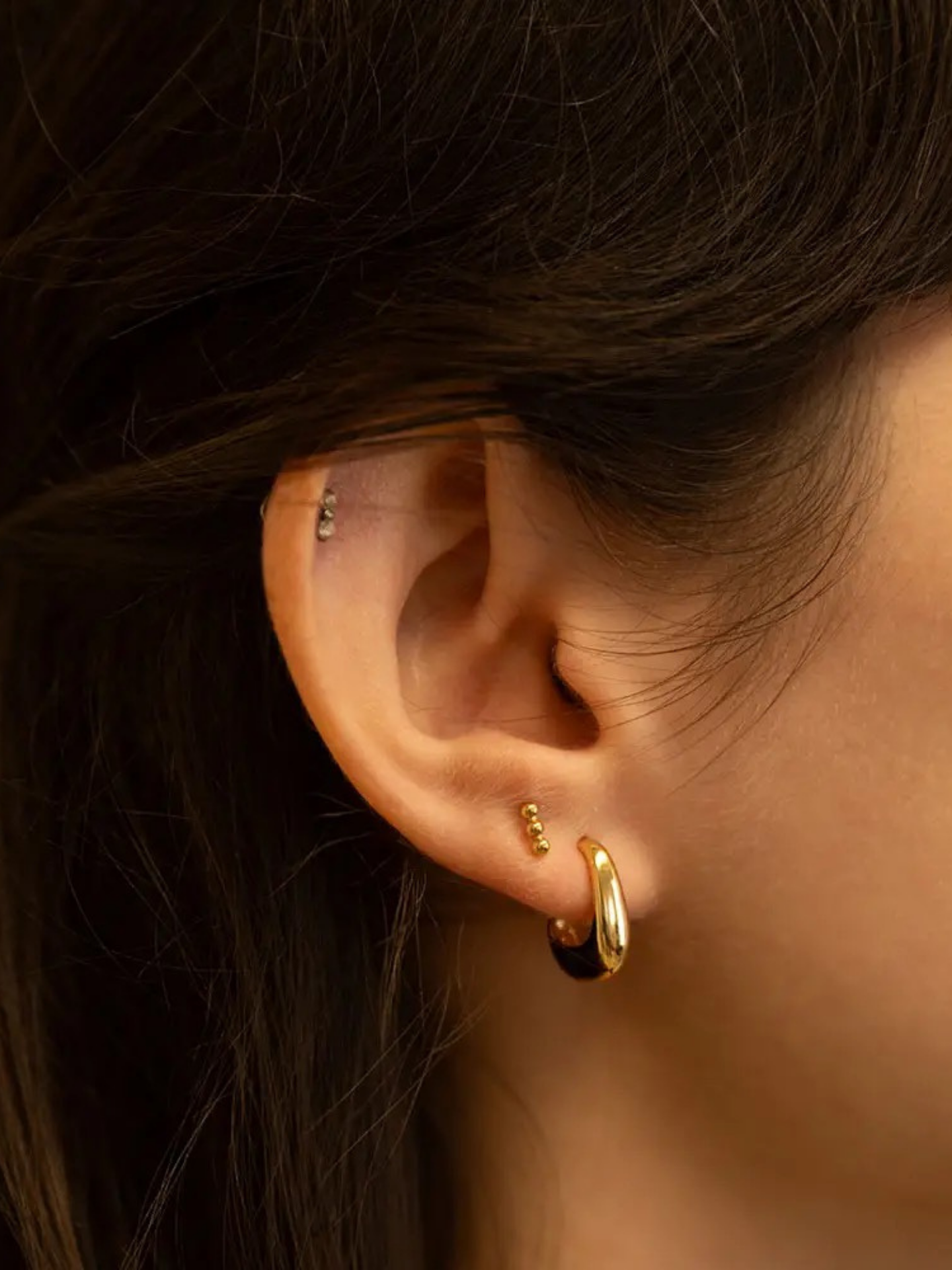 A pair of delicate rose-shaped earrings by Amano Studios with intricate petal details and silver hooks displayed against a white background.