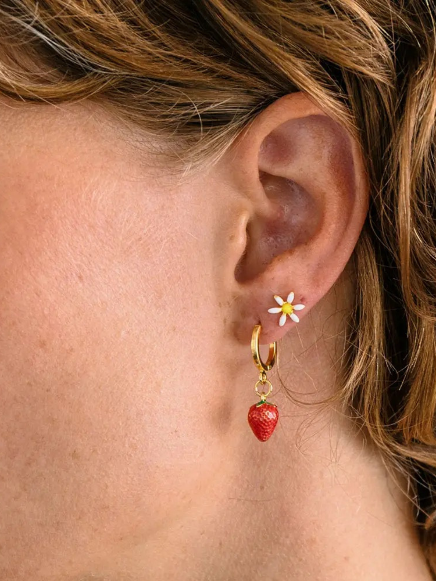 A pair of berry-shaped earrings with red and green accents from Amano Studios, hanging on display.