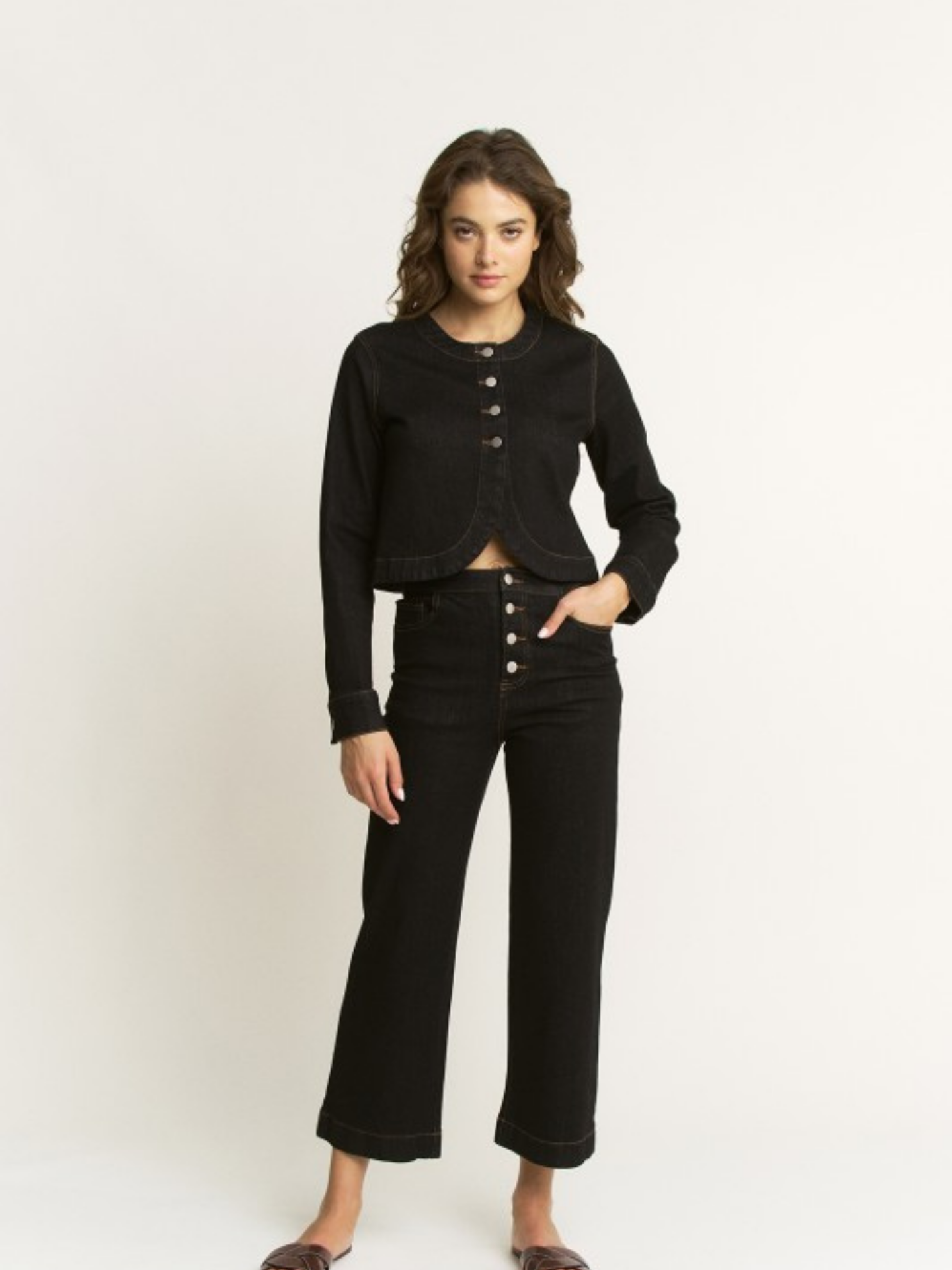 Woman wearing a black button-up top and black pants on a white background