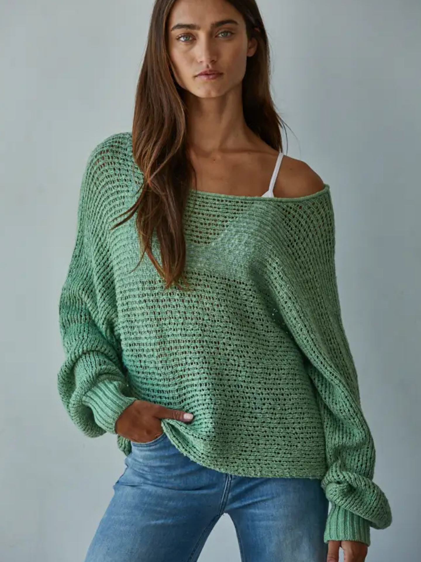 Woman wearing a green knitted sweater and blue jeans against a gray background