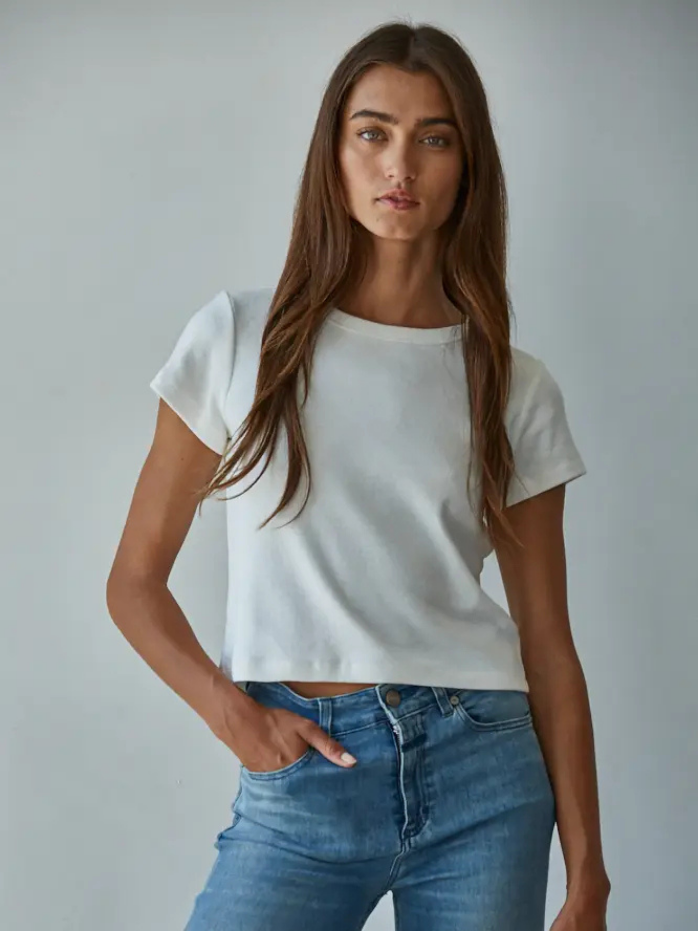 Woman wearing a white crop top and blue jeans against a plain background