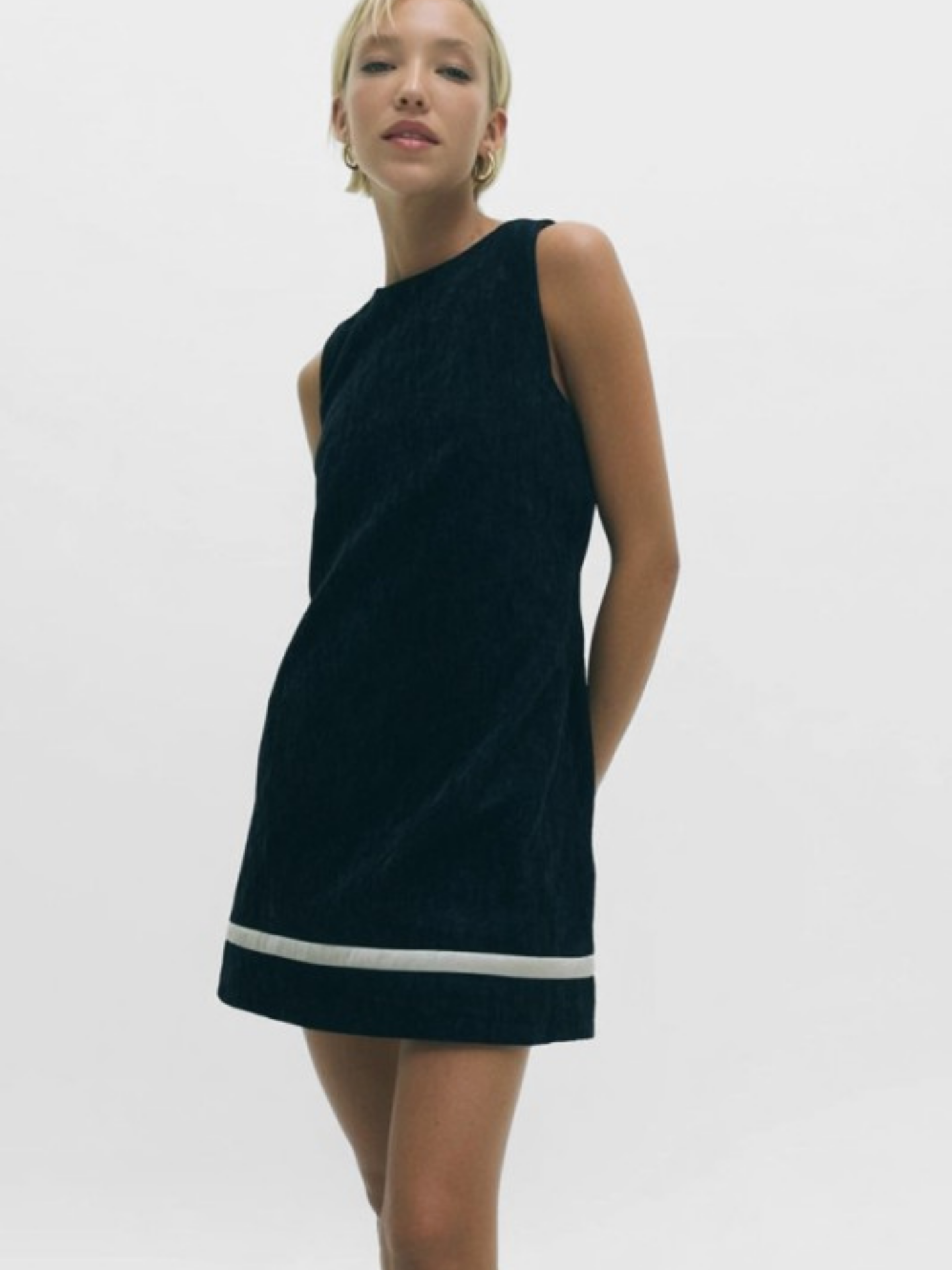 Woman wearing a black dress with a white trim on a plain background