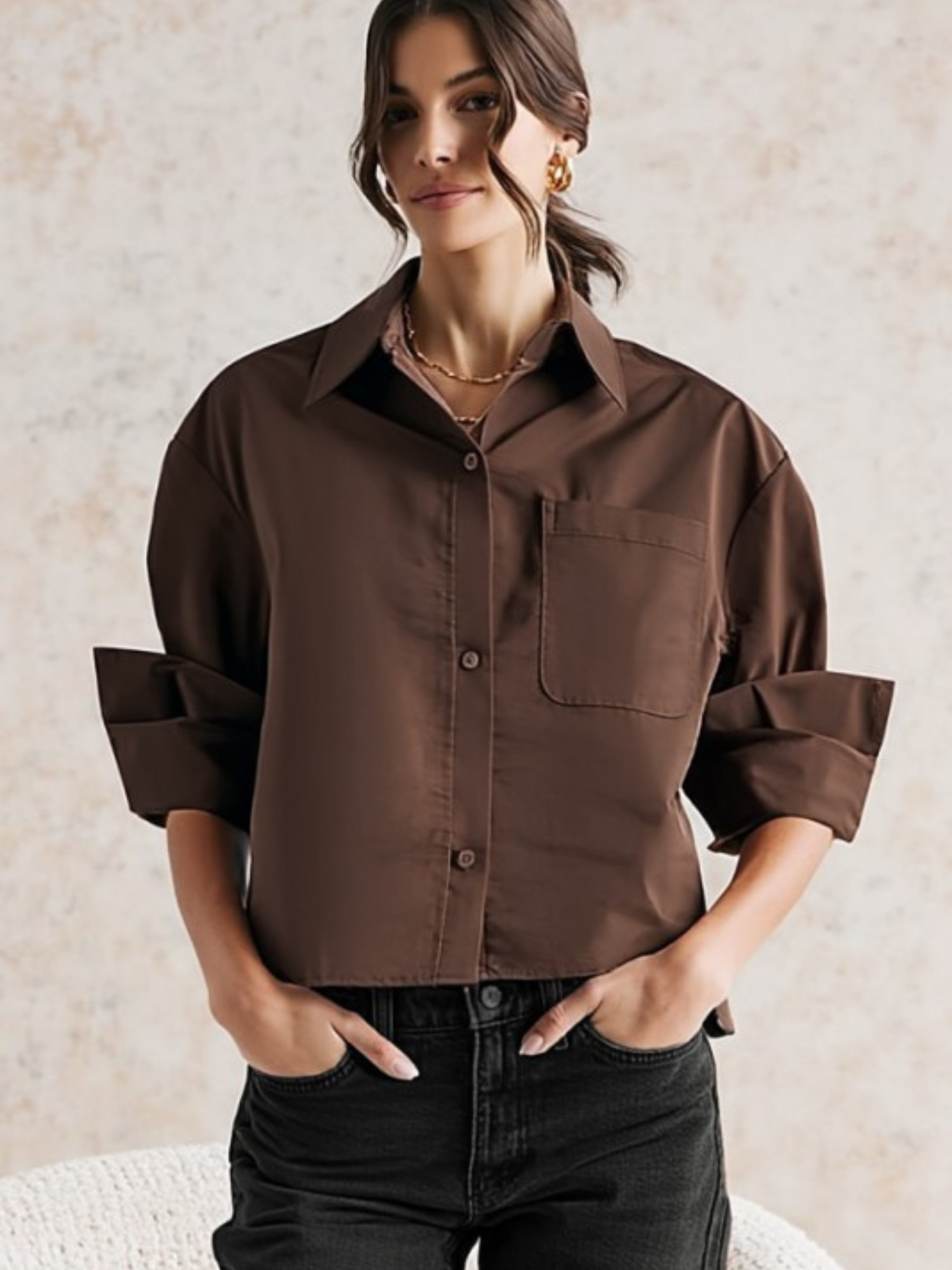 Woman wearing a brown shirt with rolled-up sleeves against a neutral background