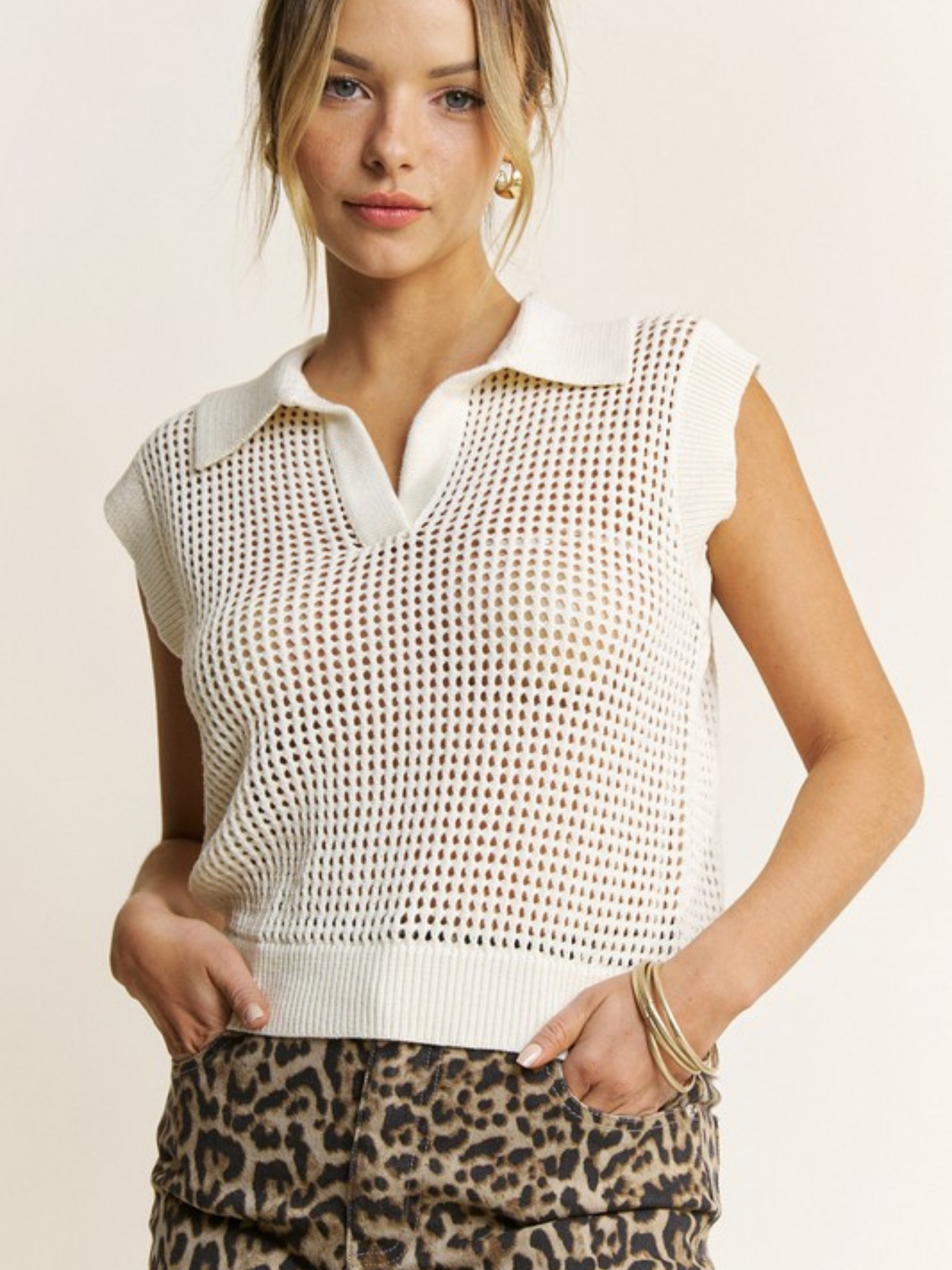 Woman wearing a white sleeveless knit top and leopard print pants on a beige background